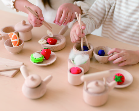 木のままごとセットのお箸で食材ぬいぐるみを掴む、子どもの写真
