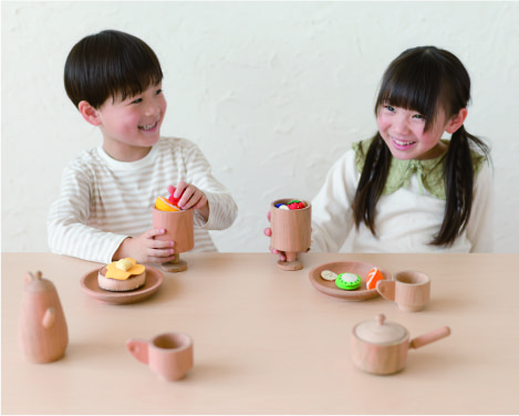 木のままごとセットで遊びながら会話する子ども2人の写真