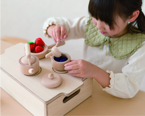 木のままごとおもちゃのお鍋で料理する子どもの画像